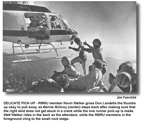 DELICATE PICK-UP  RMRU member Kevin Walker gives Don Landells the thumbs up okay to pull away, as Bernie McIlvoy (center) steps back after making sure that the right skid does not get stuck in a crack while the one runner pick-up is made. Walt Walker rides in the back as the attendant, while the RMRU members in the foreground cling to the small rock ledge. (photo by Jim Fairchild)