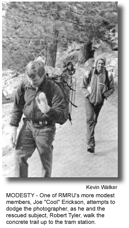 MODESTY - One of RMRU's more modest members, Joe "Cool" Erickson, attempts to dodge the photographer, as he and the rescued subject, Robert Tyler, walk the concrete trail up to the tram station. (photo by Kevin Walker)