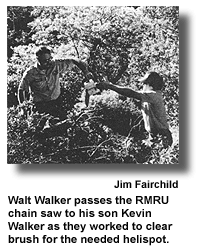 Walt Walker passes the RMRU chain saw to his son Kevin Walker as they worked to clear brush for the needed helispot. (photo by Jim Fairchild)