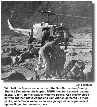 With half the Scouts loaded aboard the San Bernardino County Sheriff s Department helicopter, RMRU members started loading packs. (L to R) Bernie McIlvoy with two packs, Walt Walker stood by with another, Steve Zappe and Tom Aldrich gathered up more packs, while Kevin Walker (who was giving Helitac signals) held up one finger, for one more pack. (photo by Jim Fairchild)
